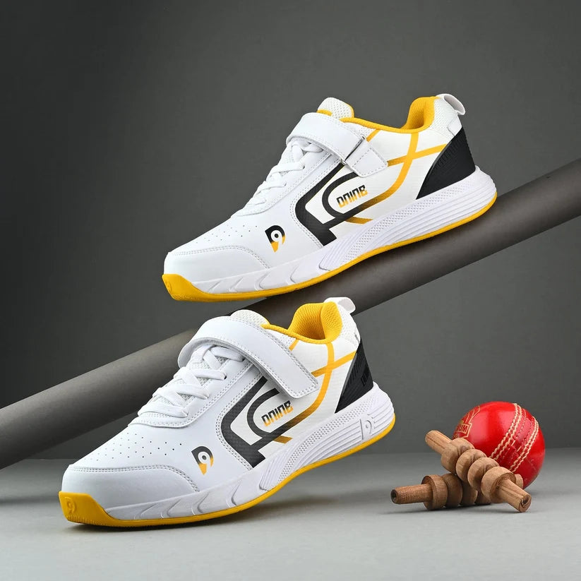 White and yellow Dnine Kings-2 cricket bowling spikes with ankle straps displayed alongside a red cricket ball and miniature wooden stumps